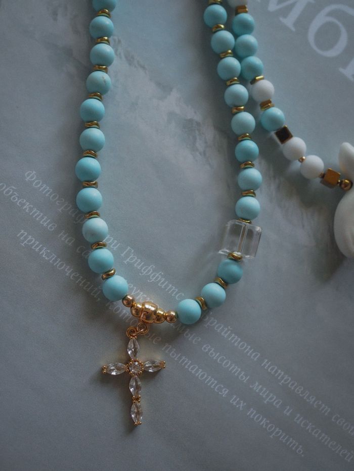 Close-up of a turquoise beaded necklace with a cross pendant, exuding elegance.